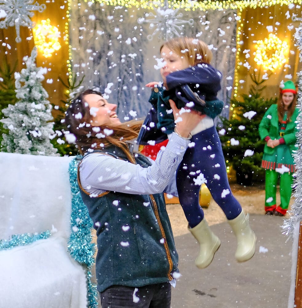 mother and daugher in farmer christmas barn with snow and lights and elf