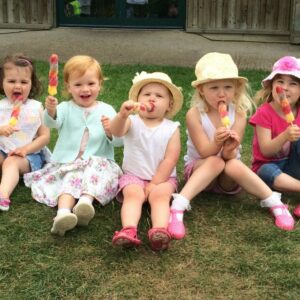 Children enjoying ice lollies sitting on a grassy bank at farmer palmers.